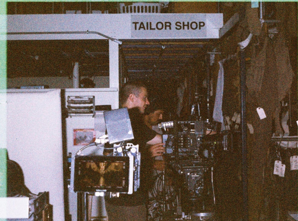 Camera operator lining up a shot under a Tailor Shop sign