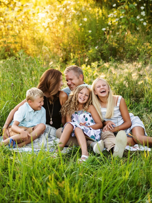 Family of five laughing together in a sunny field, representing natural and joyful family photography.
