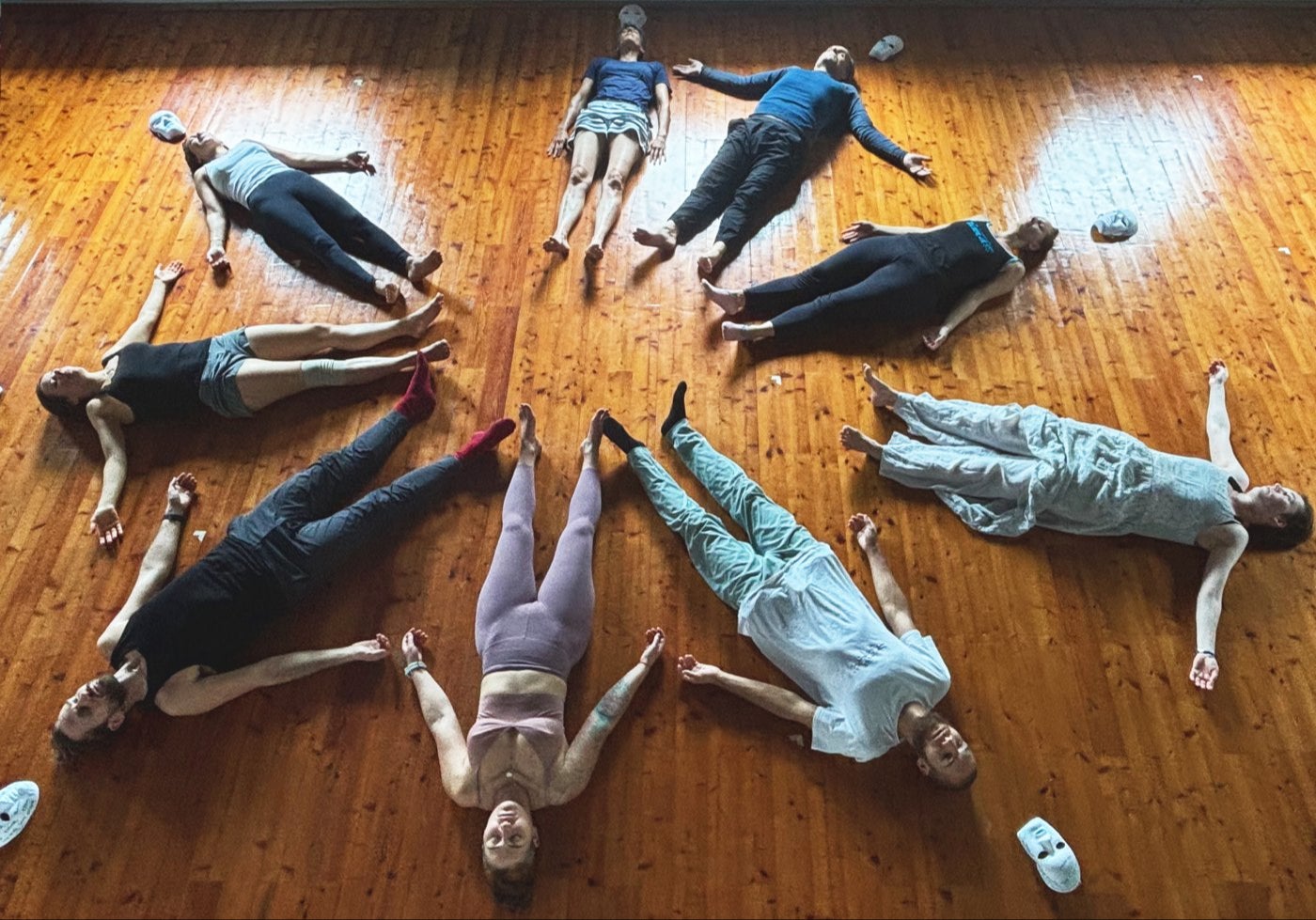Guests lying on the wooden floor in a star shape, feet together, with white masks around them