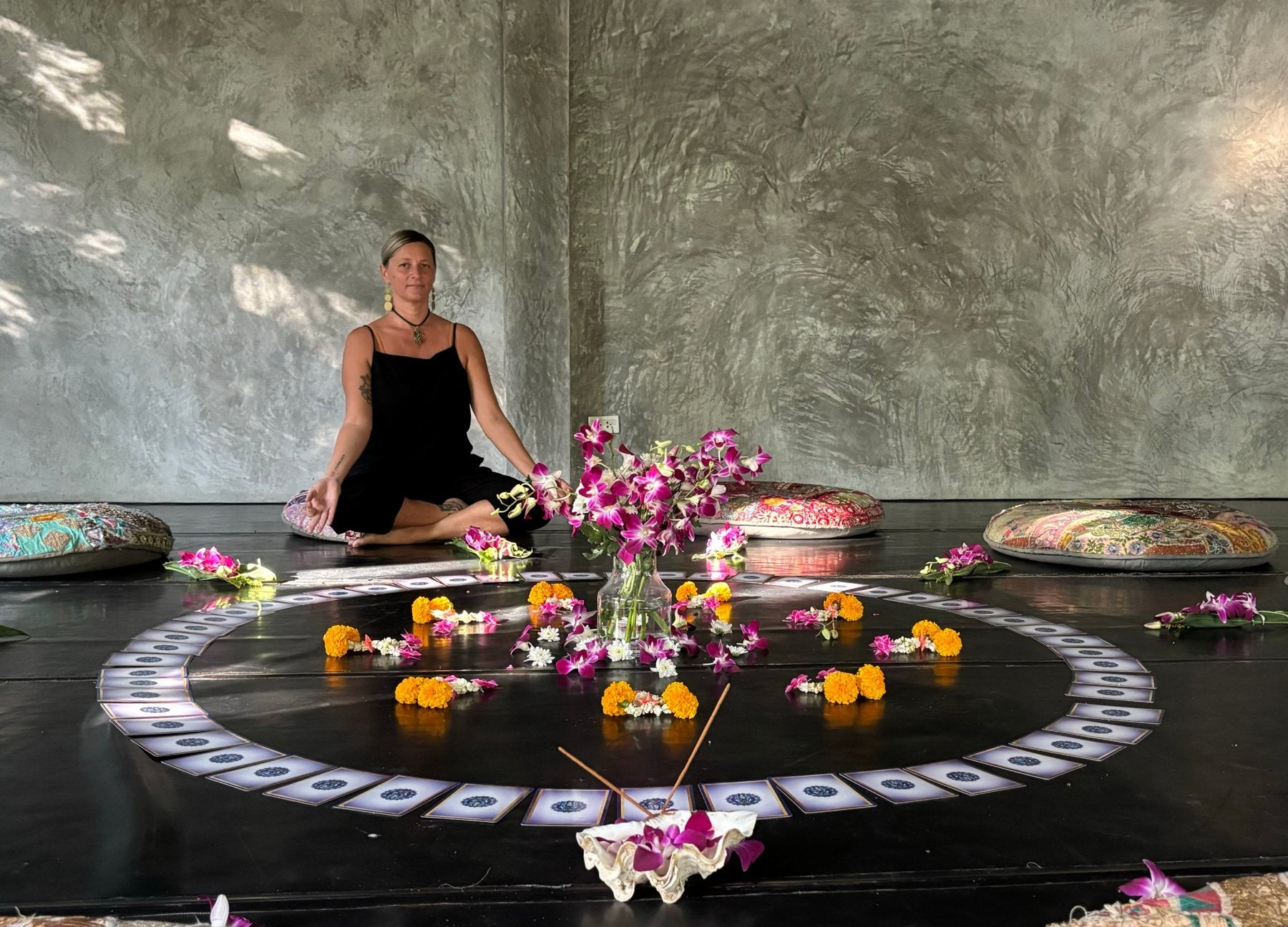 Clelia seated in meditation beside a ritual circle of cards, flowers and incense laid out on the floor