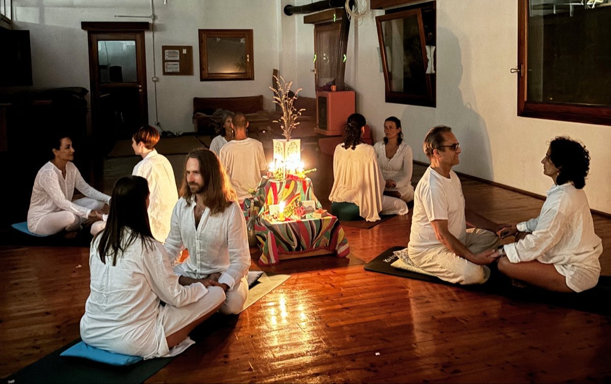 Guests in white sitting in pairs, holding hands, around a candlelit altar during an evening ritual