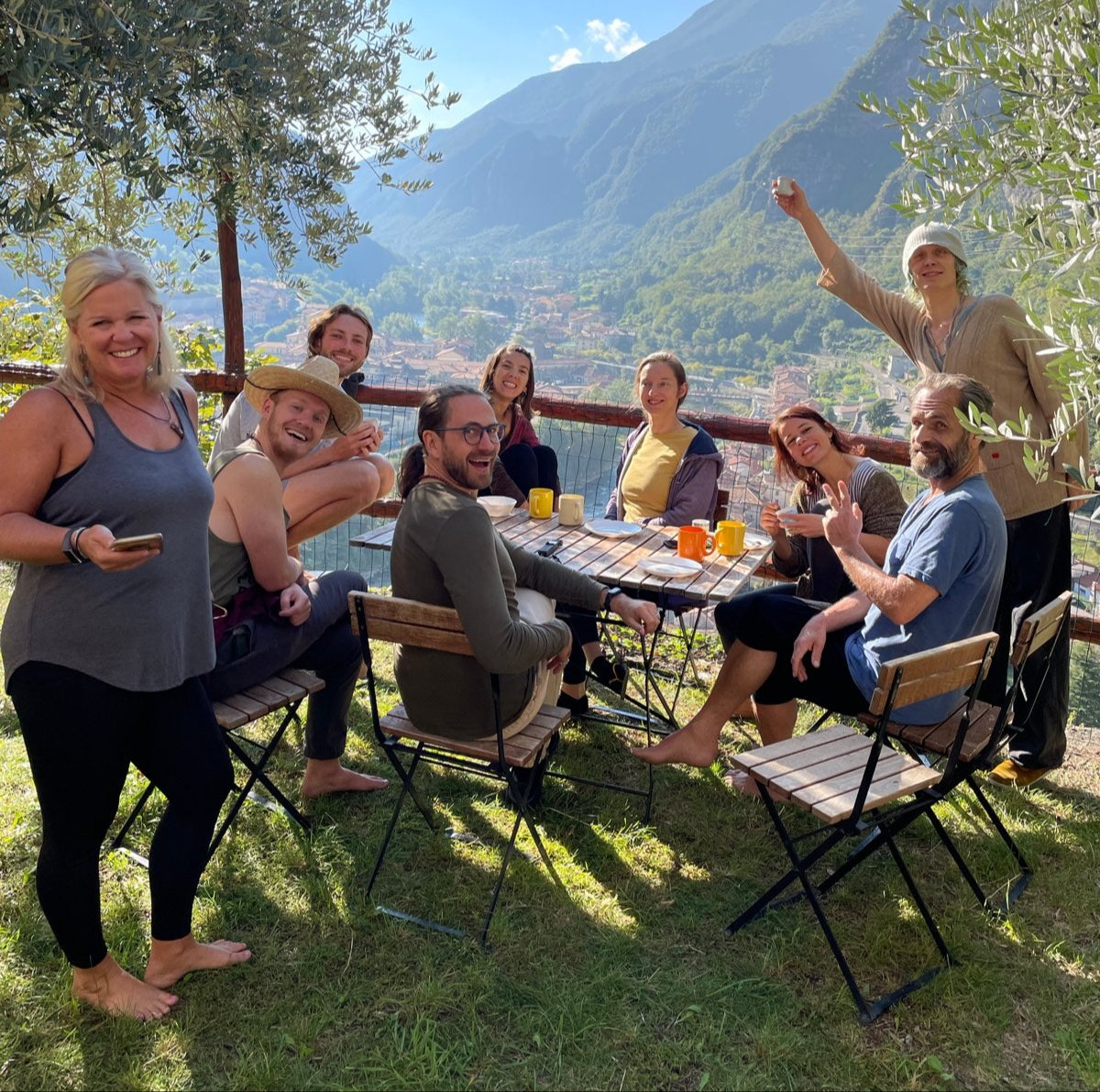 Guests laughing around a table under the olive trees, mountains and valley behind them
