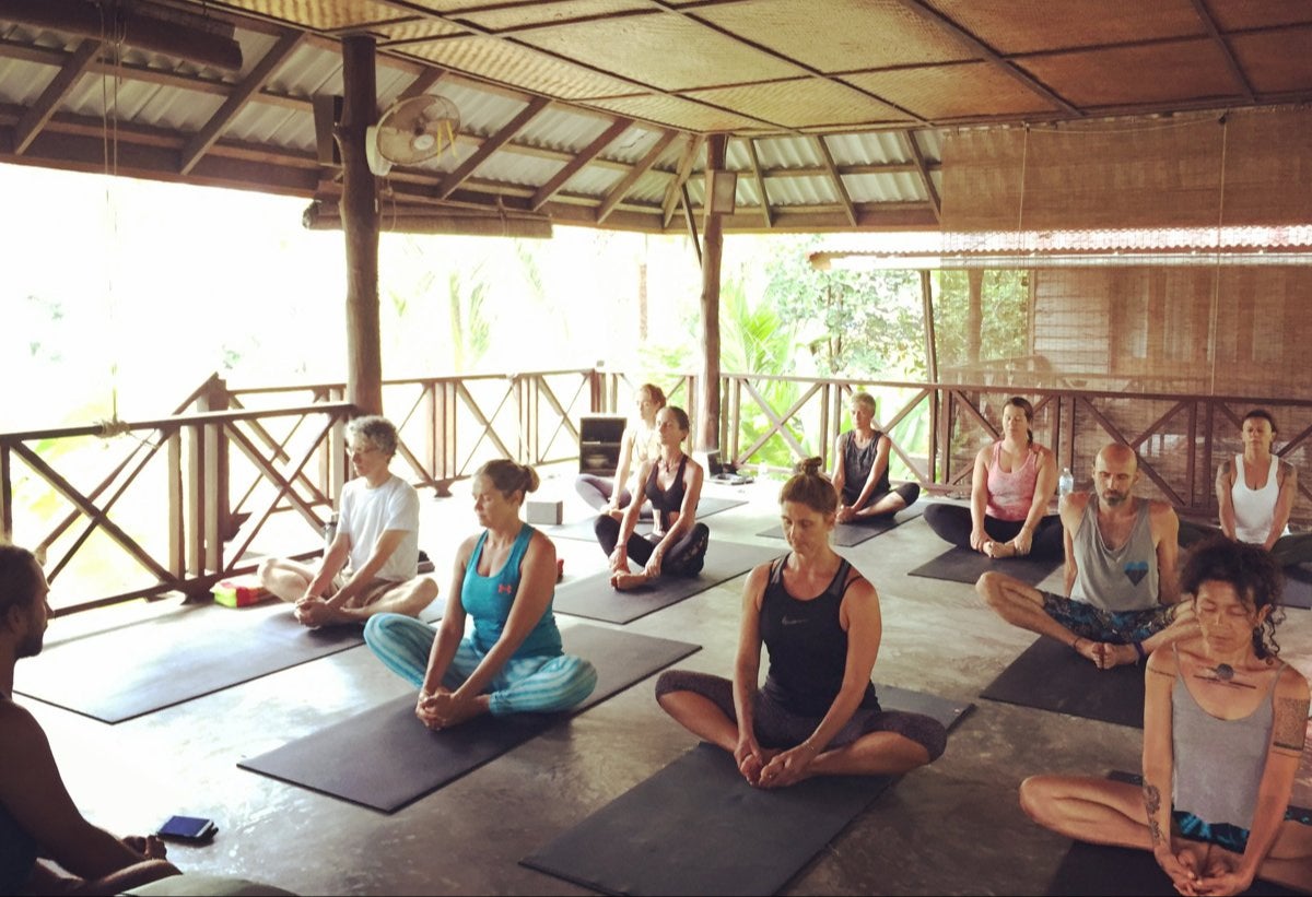 A group seated on their mats with eyes closed in an open-air yoga pavilion