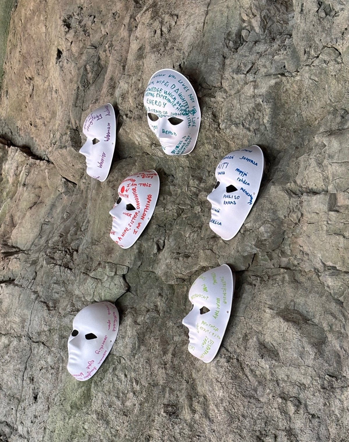 Six white masks on a rock face, each covered in the words guests wrote about the roles they play