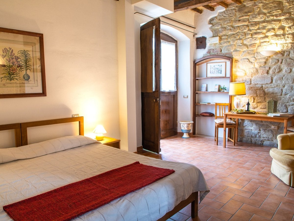 A bright double room with terracotta floor, stone wall and a small reading corner