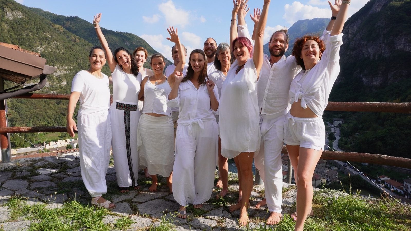 The Inner Alchemy group in white, arms raised, on a terrace in the mountains