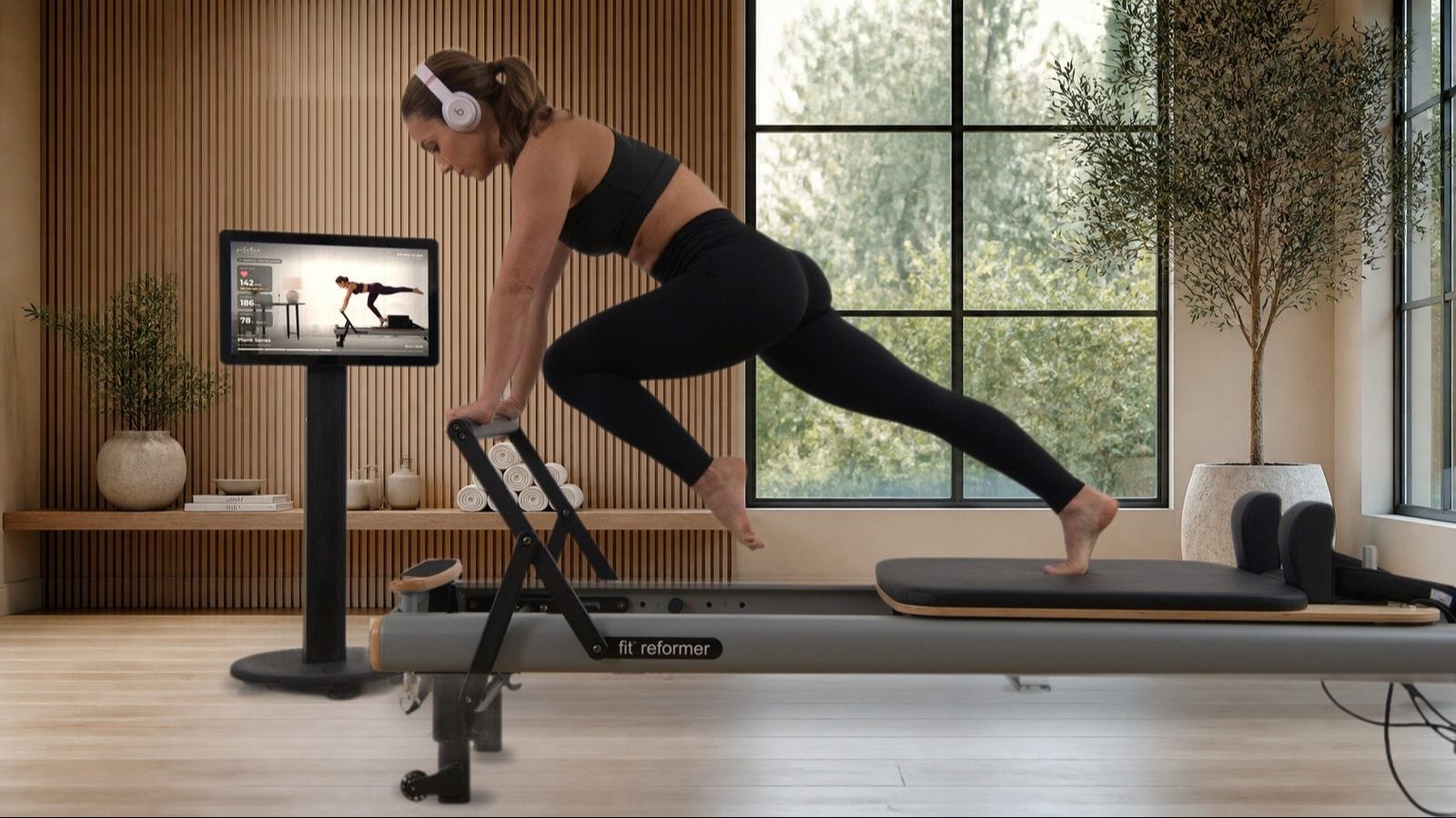 Maghan training on a fit reformer beside the StudioConnect® kiosk in a boutique Pilates studio, with heart rate, calories and intensity on screen