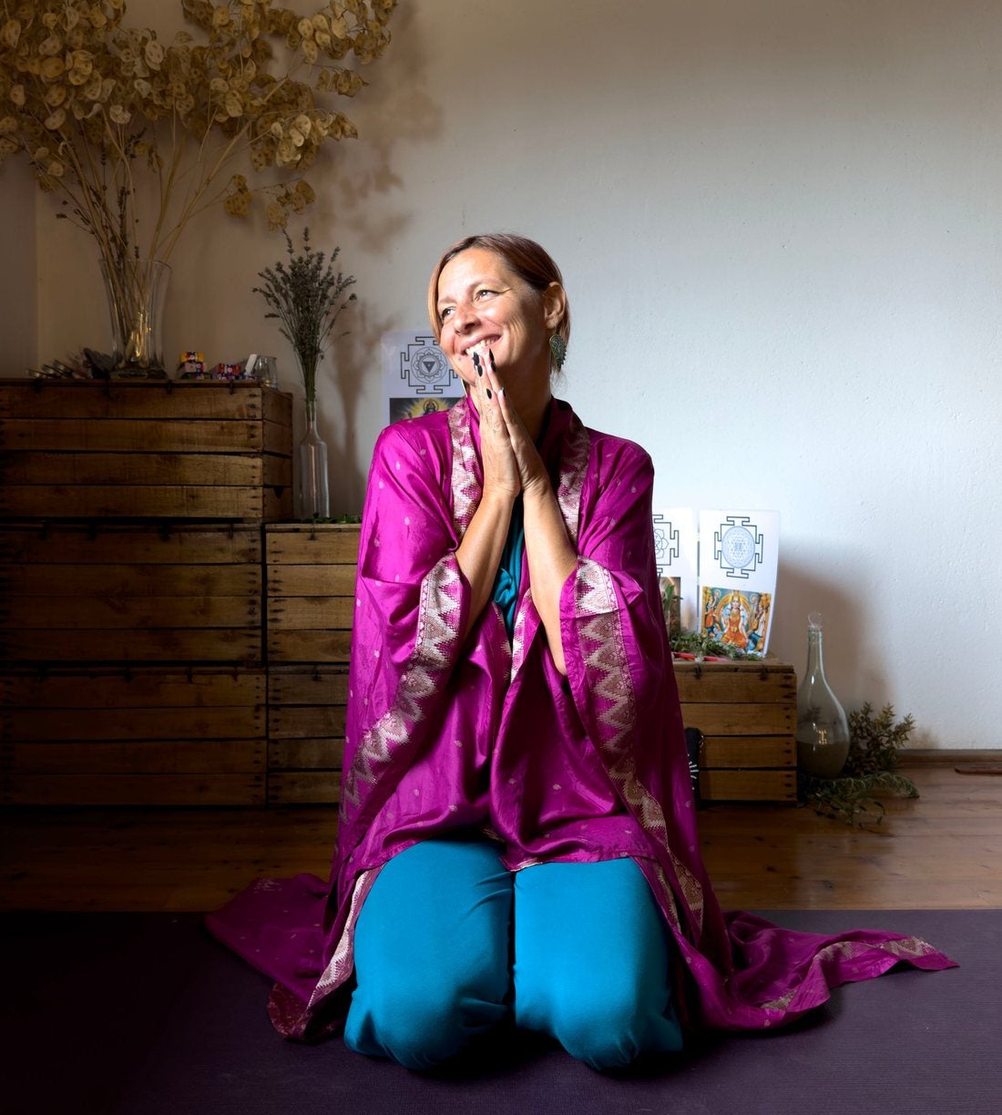 Clelia kneeling on her mat in a magenta silk wrap, smiling, hands in prayer